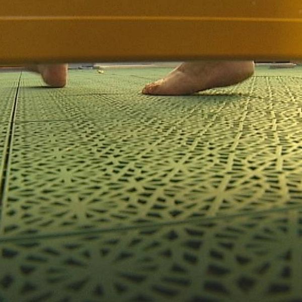 Fötter på badrumsgolv fotograferade i springan under en skärmvägg.