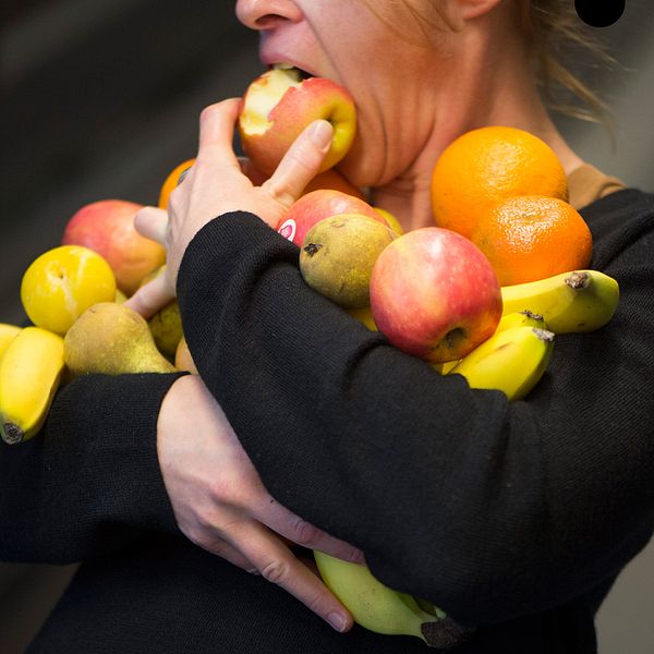 Kvinna med famnen full av frukt tar en tugga ur ett äpple