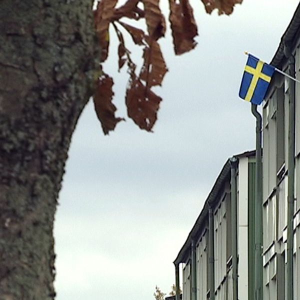 Lägenhetshus utifrån med svensk flagga vajande från en balkong.