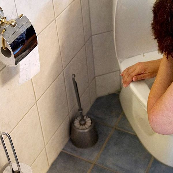En kvinna står böjd över en toalett.