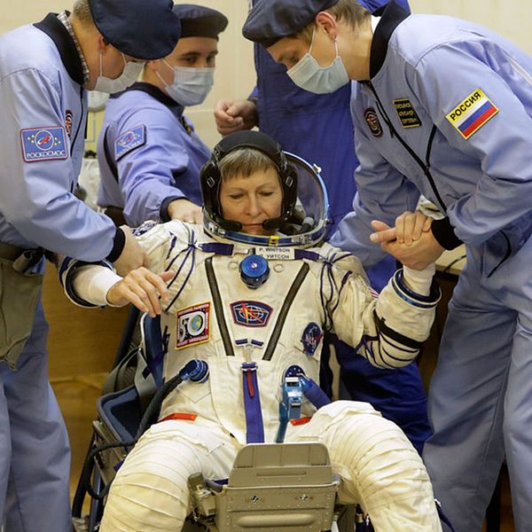 Astronauten Peggy Whitson, en av besättningsmedlemmarna på ISS, får hjälp att resa sig efter att hennes rymddräkt inspekterats före avfärden från Baikonur.