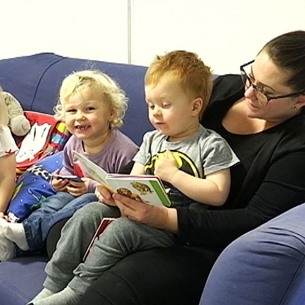 Tre barn sitter tillsammans med sin förskolelärare och läser böcker.