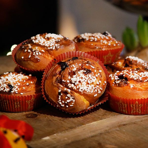 Färdiggräddade bullar dekorerade med pärlsocker i pappersformar ligger på skärbräda av trä.