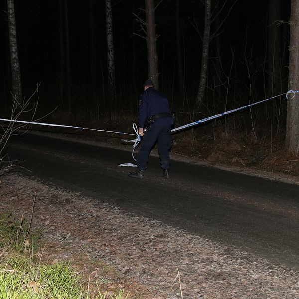 En polis som sätter upp ett avspärrningsband på en liten grusväg.