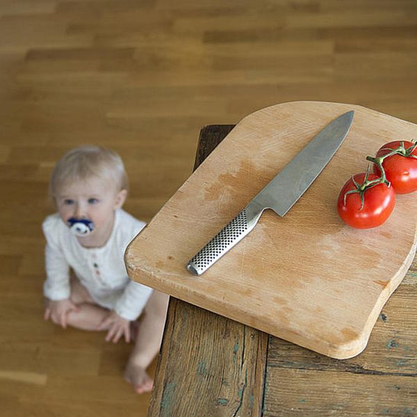 Faror i hemmet för små barn. En bebis riskerar att få tag på en vass kniv hemma i köket.