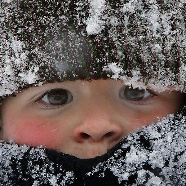närbild på litet barn med stor mössa och halsduk, snöig