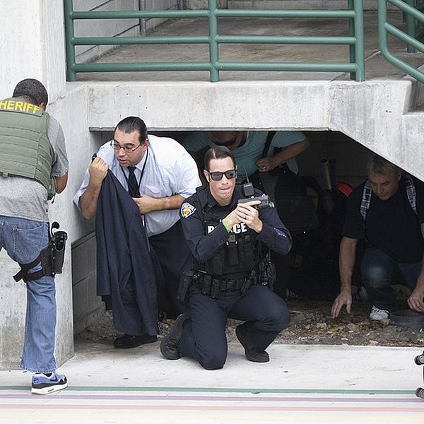 En polis som tar skydd vid en trappa håller i ett vapen.