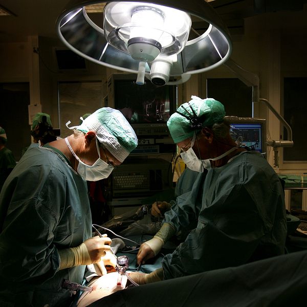 Två personer i operationskläder står över ett operationsbord med patient