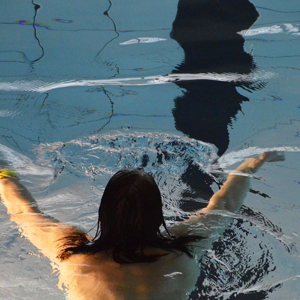 Kvinna sedd uppifrån simmar i en bassäng.