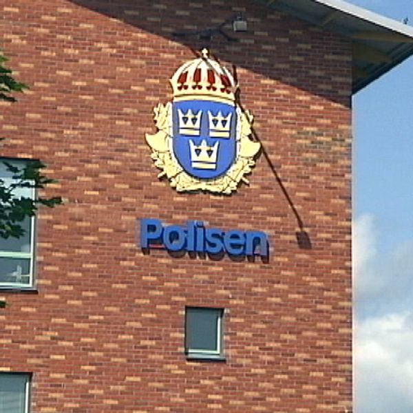 Polishuset i Karlstad med löv i förgrunden, emblem på fasaden, sommartid