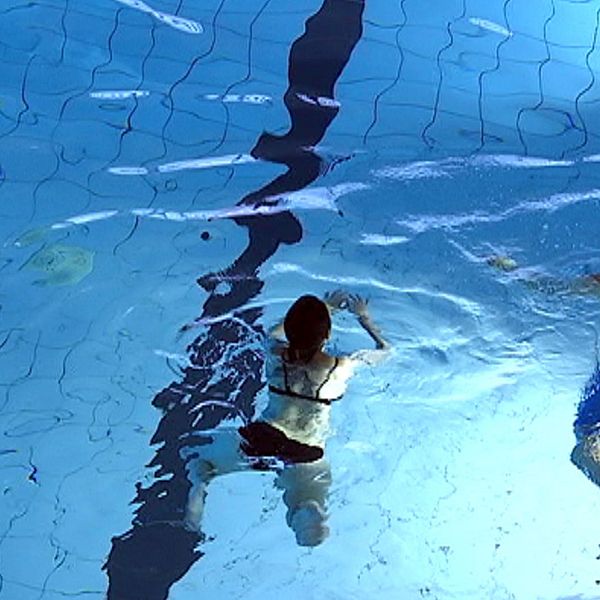 Två personer simmar i en simbassäng.