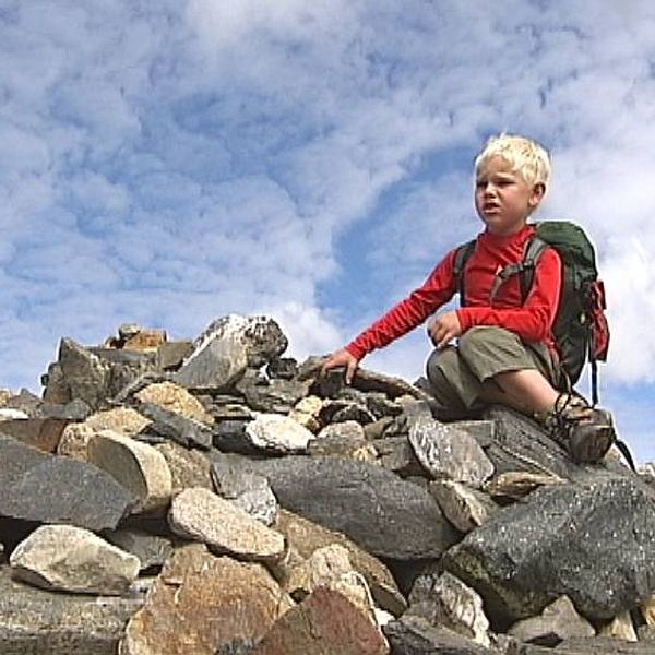 Pojke sitter på stenröse i Fjällen