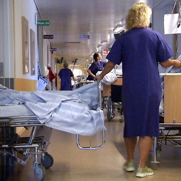 En sjuksköterska flyttar två sängar med patienter i en sjukhuskorridor.