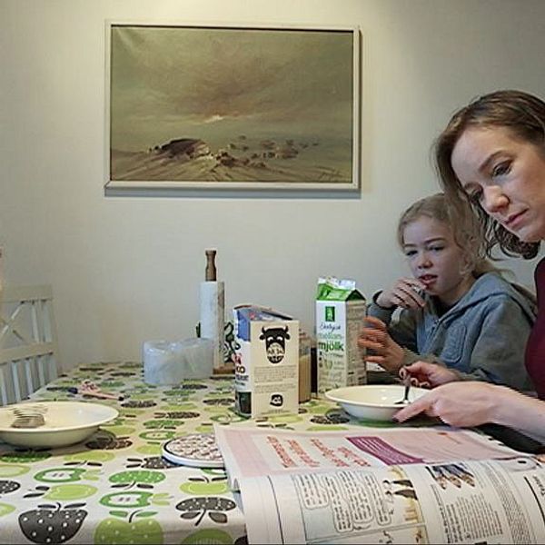 Två barn äter frukost med sin mamma som läser tidningen och äter frukost.