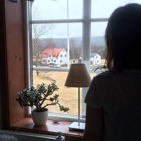 Ung kvinna står och tittar ut genom fönster.