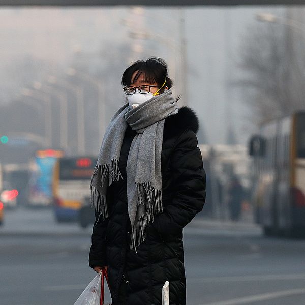 En kvinna i andningsmask står på en gata i Peking, Kina.