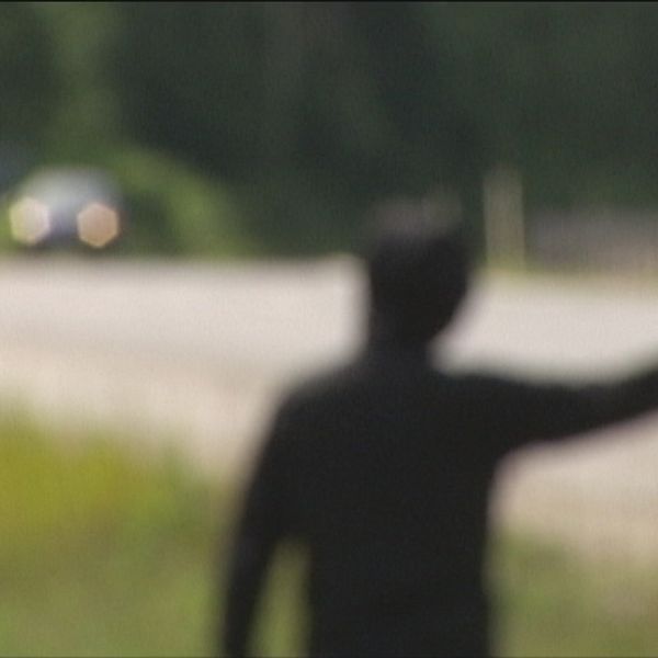 Anonym och suddig bild bakifrån, en svartklädd person viftar åt två bilar som kommer körande mot personen.