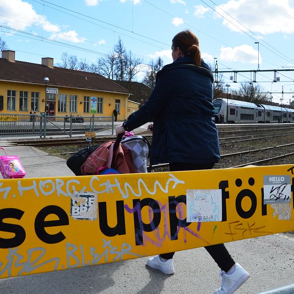 Familj passerar över spåret vid Södra station i Örebro. I förgrunden en skylt med texten ”se upp för tåg”.