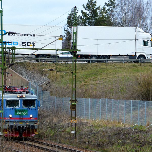 Ett tåg passerar i en tunnel under en väg. Ovanför färdas en lastbil.