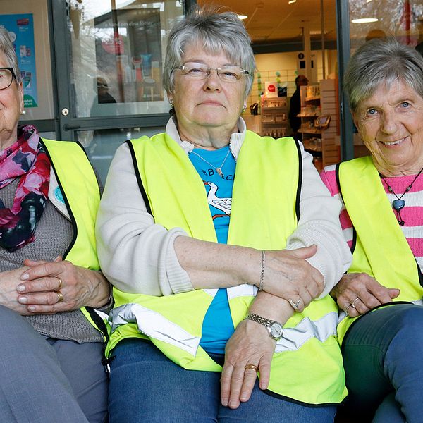 tre äldre kvinnor med varselvästar sitter på bänk