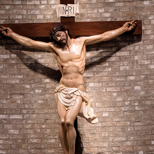 Bild på en staty vid en tegelvägg (förmodligen i en kyrka), där Jesus hänger på korset. Ovanför står det INRI på latin, vilket är en akronym för ”Jesus från Nasaret, judarnas konung”.