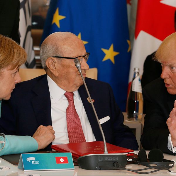 Tysklands förbundskansler Angela Merkel i turkos dräkt för livliga diskussioner med USA:s president Donald Trump i röd slips. Tunisiens president sitter mellan dem och följer samtalet.