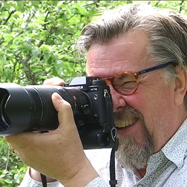 Fotografen Lars Dahlström står i prickig skjorta och tittar in i en kamera.