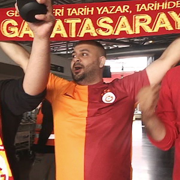 tre sjungande, glada turkiska män i klubbtröjor och med banderoll