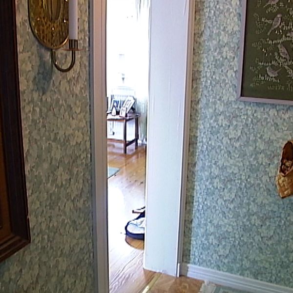 Ett rum med en blommig tapet och ett par nävertofflor hänger på en vägg.