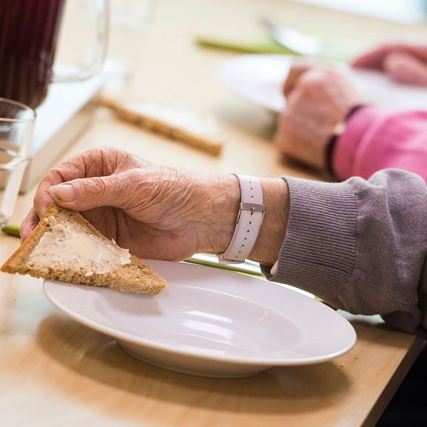Äldre kvinna håller en smörgås i handen.
