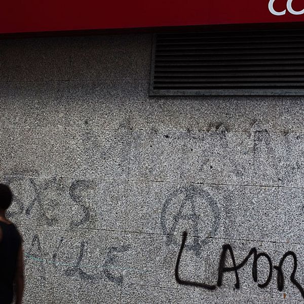 En pojke passerar en spansk bank. ”Tjuvar” står det klottrat på bankens vägg.