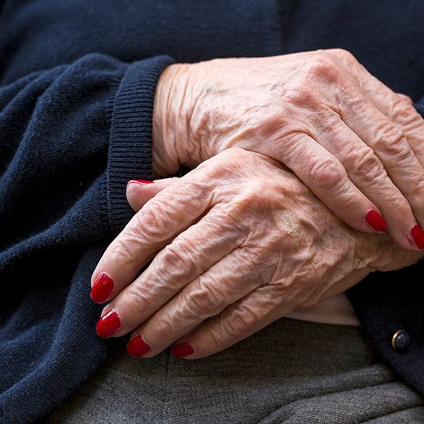 Äldre kvinnas händer med rött nagellack.