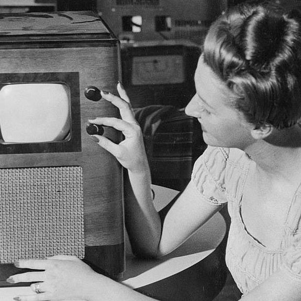 Svartvit bild av en kvinna som vrider på kanalratt på gammaldags tv.