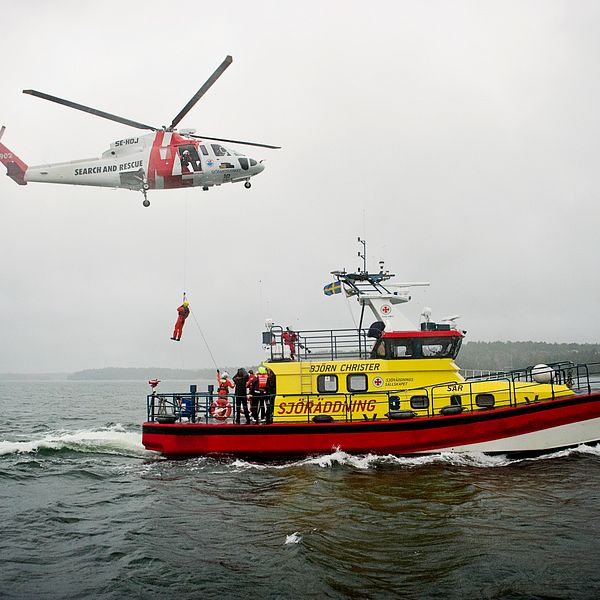 Sjöräddningssällskapets båt ute på vatten. Ovanför flyger en helikopter.