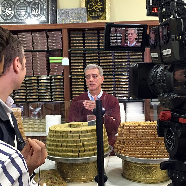 Salim Sakka vid konditoridisken med tårtfat av baklava staplade på varandra.