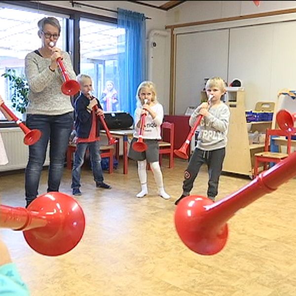 Barn och förskolepedagog spelar blåsinstrumentet pbuzz.