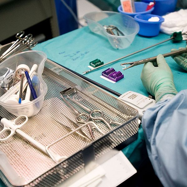 Ett bord med verktyg i en operationssal. En läkares händer iförda gröna plasthandskar håller i ett verktyg.