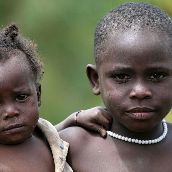 En flicka bär sin yngre syster på armen i en by i västra Uganda. Bland de ”osynliga”, som främst lever i Afrika och Asien, är mer än en tredjedel barn som inte har registrerats vid födseln.