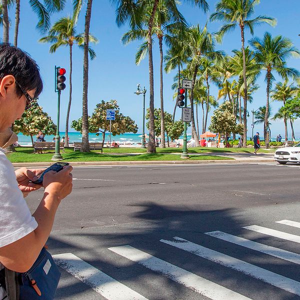 Arkivbild: En person kollar i mobilen när han korsar vägen i Honolulu, Hawaii. Något som han skulle kunna få böter för.