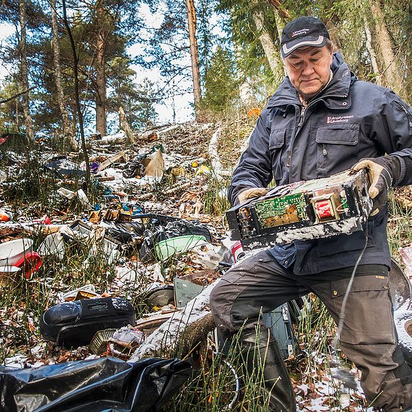 Naturbevakaren Anders Berglund står bland mängderna av sopor som har slängts i naturreservatet. I handen har han lyft upp en gammal dator.