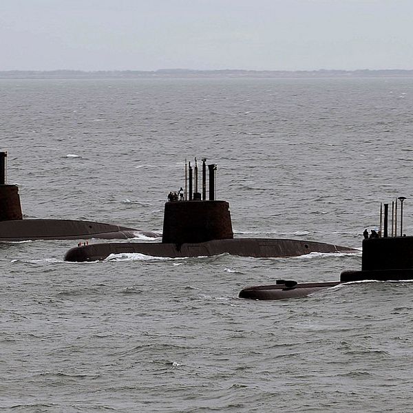 Tre ubåtar som stigit upp till ytan syns på rad i havet.