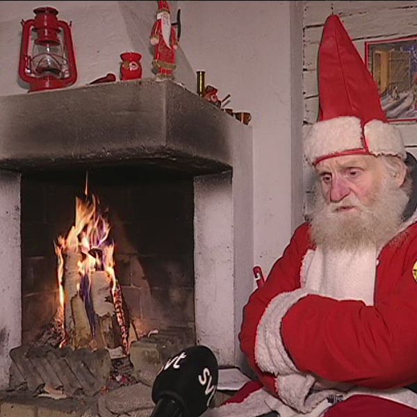 en äldre man utklädd till tomte som sitter deppig vid öppen spis