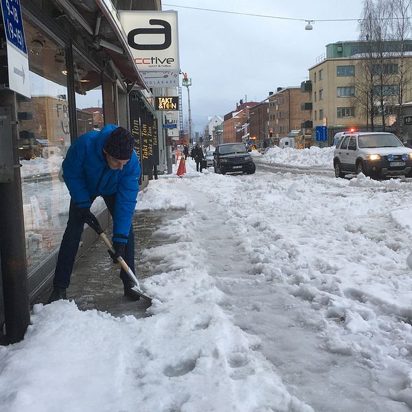 Man skottar bort snö o vatten vid port på Kungsgatan Luleå