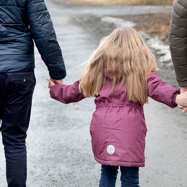 Två pappor går hand i hand med sin dotter
