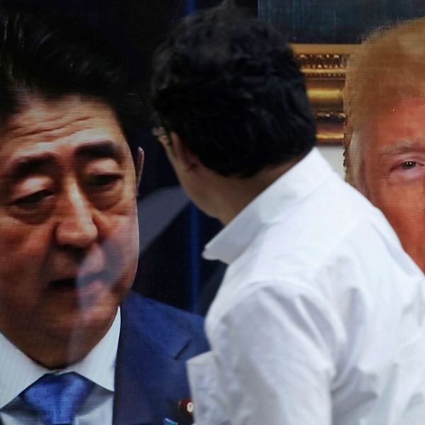 En man framför Shinzo Abe och Donald Trump på skärmar i Tokyo