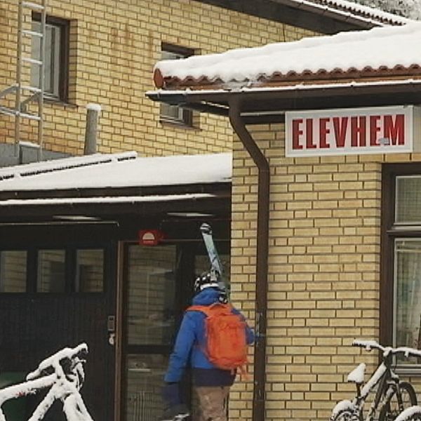 person bär skidor mot entre på byggnad med skylten ”elevhem”