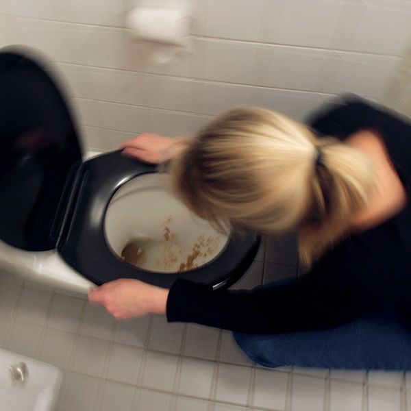 En kvinna spyr i en toalett.