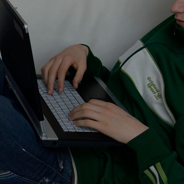 En pojke sitter med en bärbar dator i knät i en soffa.