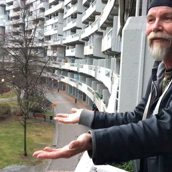 Kenneth Forsman står med utslagna händer mot ett litet grönområde intill ett stort antal lägenheter