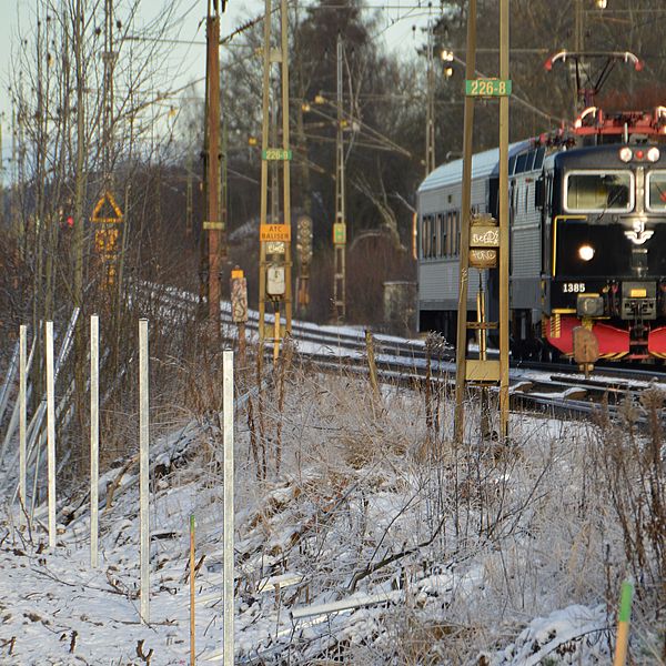 Stängsling av järnväg. Skyddande staket sätts upp, svart lok passerar.